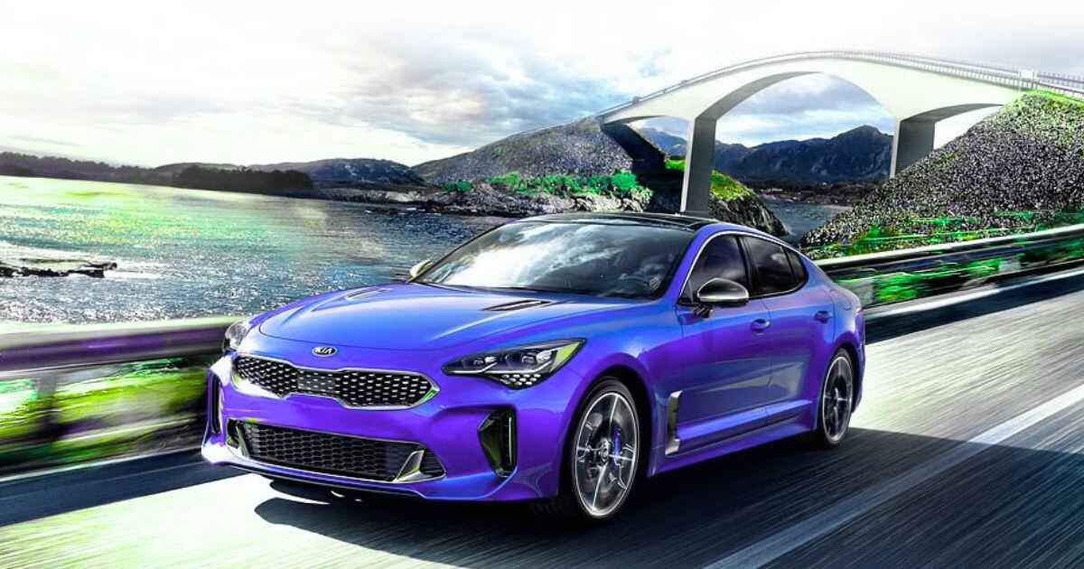 A blue Kia Stinger is driving on the road near the beach in the afternoon.
