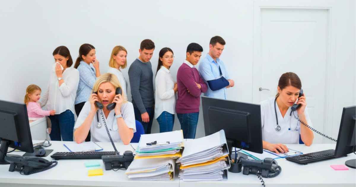 Why Small Medical Practices Struggle to Answer Their Phones 1 Overwhelmed medical receptionists juggling phone calls and patient check-ins at a small clinic front desk, showing why medical practices struggle to answer their phones.