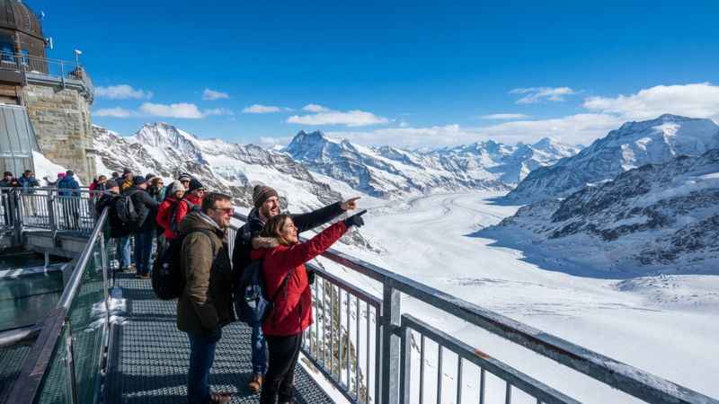 Visitors enjoying panoramic views of the Aletsch Glacier from the Sphinx Observation Deck at Jungfraujoch in Switzerland.